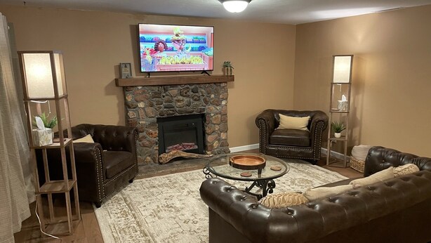 A living room with a stone fireplace, leather sofas, a coffee table, and a television mounted above the fireplace.