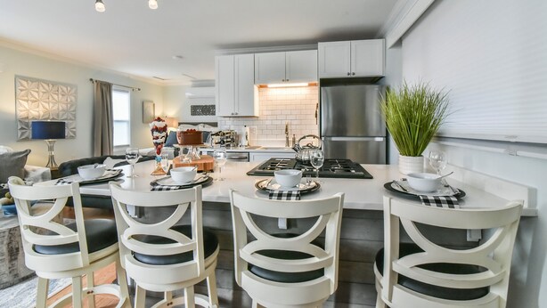 A modern kitchen with white cabinetry, a central island with seating, and a stainless steel refrigerator.