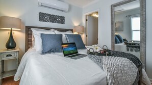 A neatly made bed with a laptop, a bedside lamp, and a decorative wall piece.