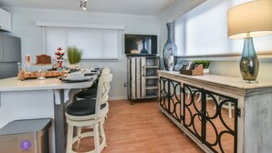 A modern kitchen with a dining area, wooden flooring, a TV, and a decorative vase.