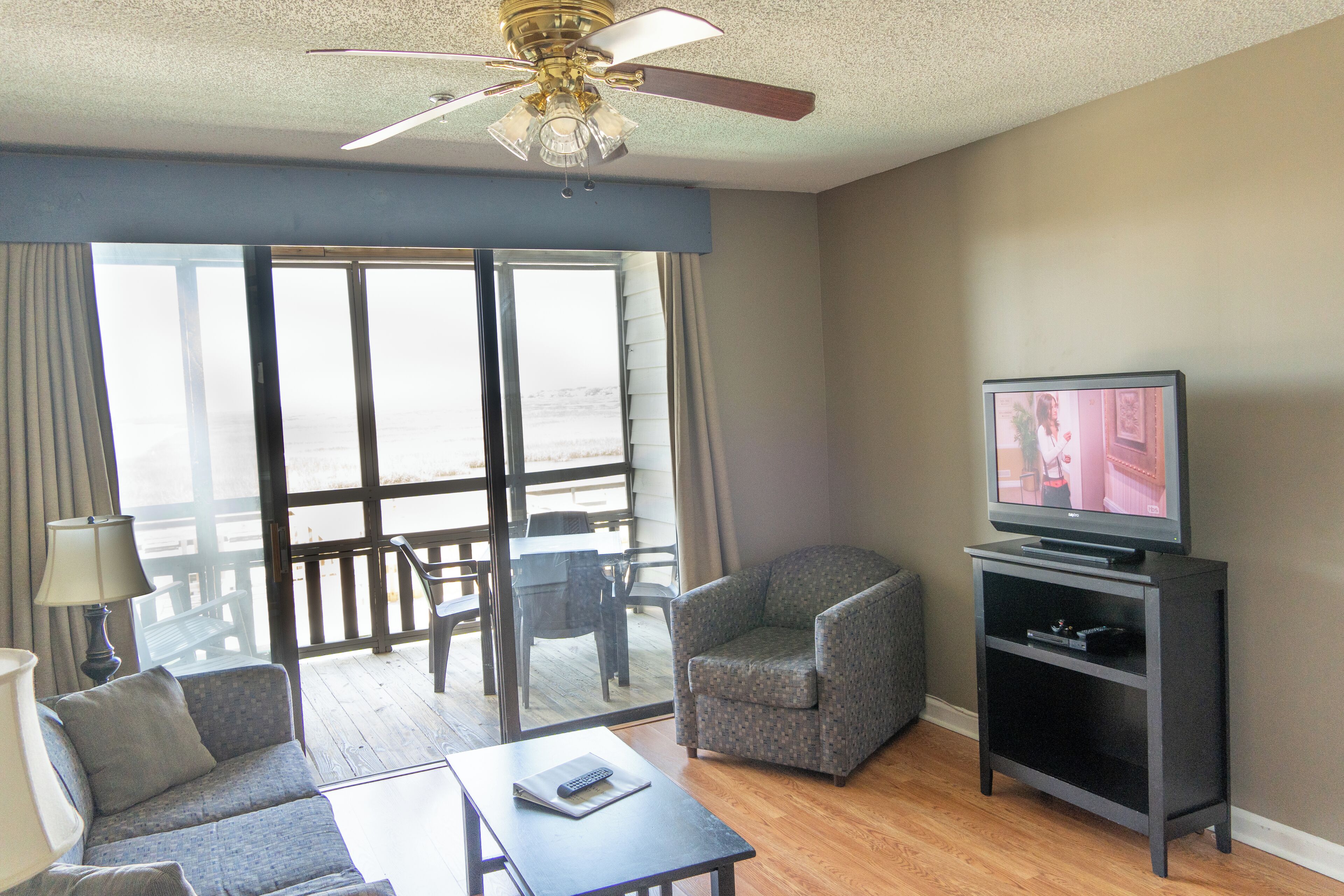 A living room with a sofa, armchair, coffee table, TV stand, and a balcony with a view.