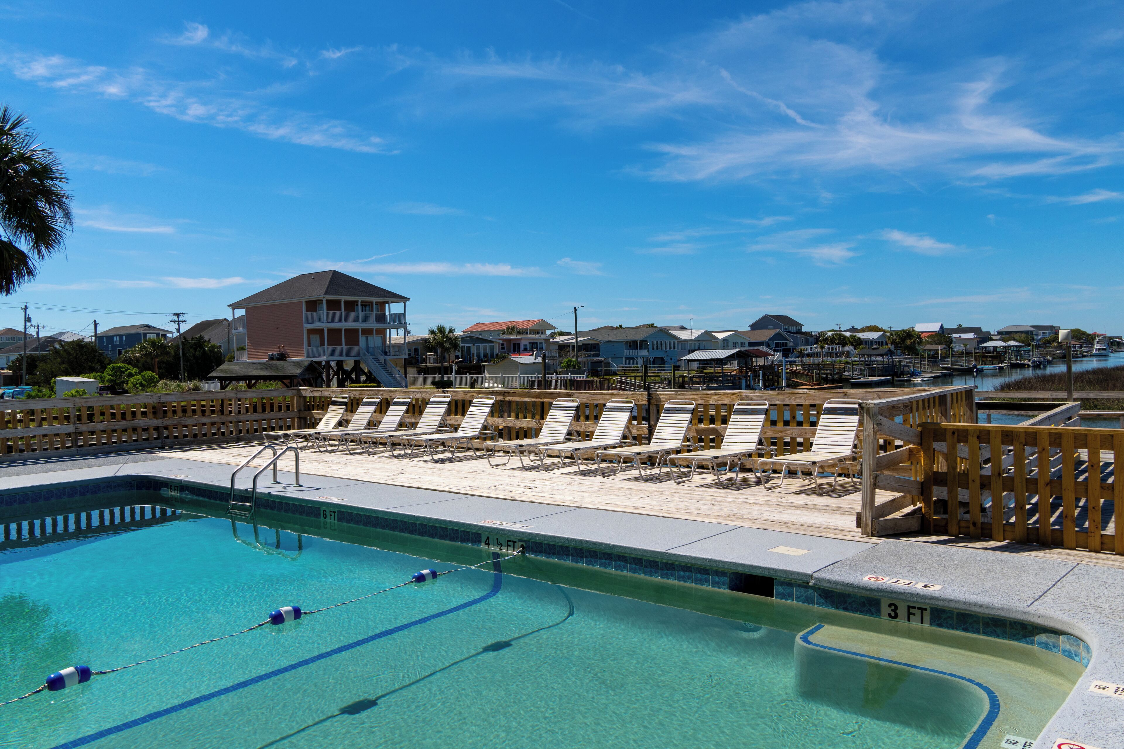 A swimming pool with clear blue water, adjacent lounge chairs, and a wooden deck.