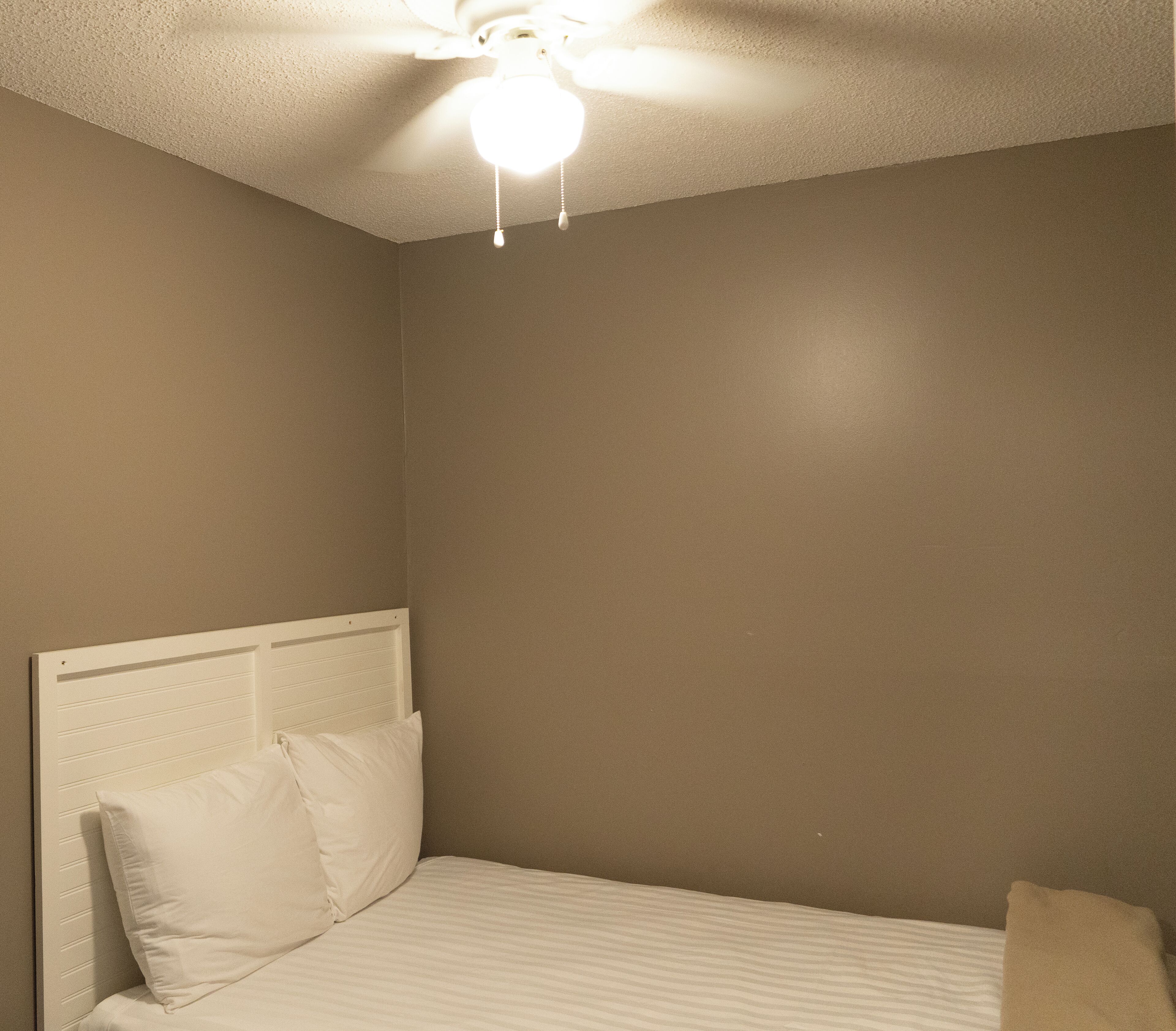 A bedroom with a single bed, white headboard, and a ceiling fan.