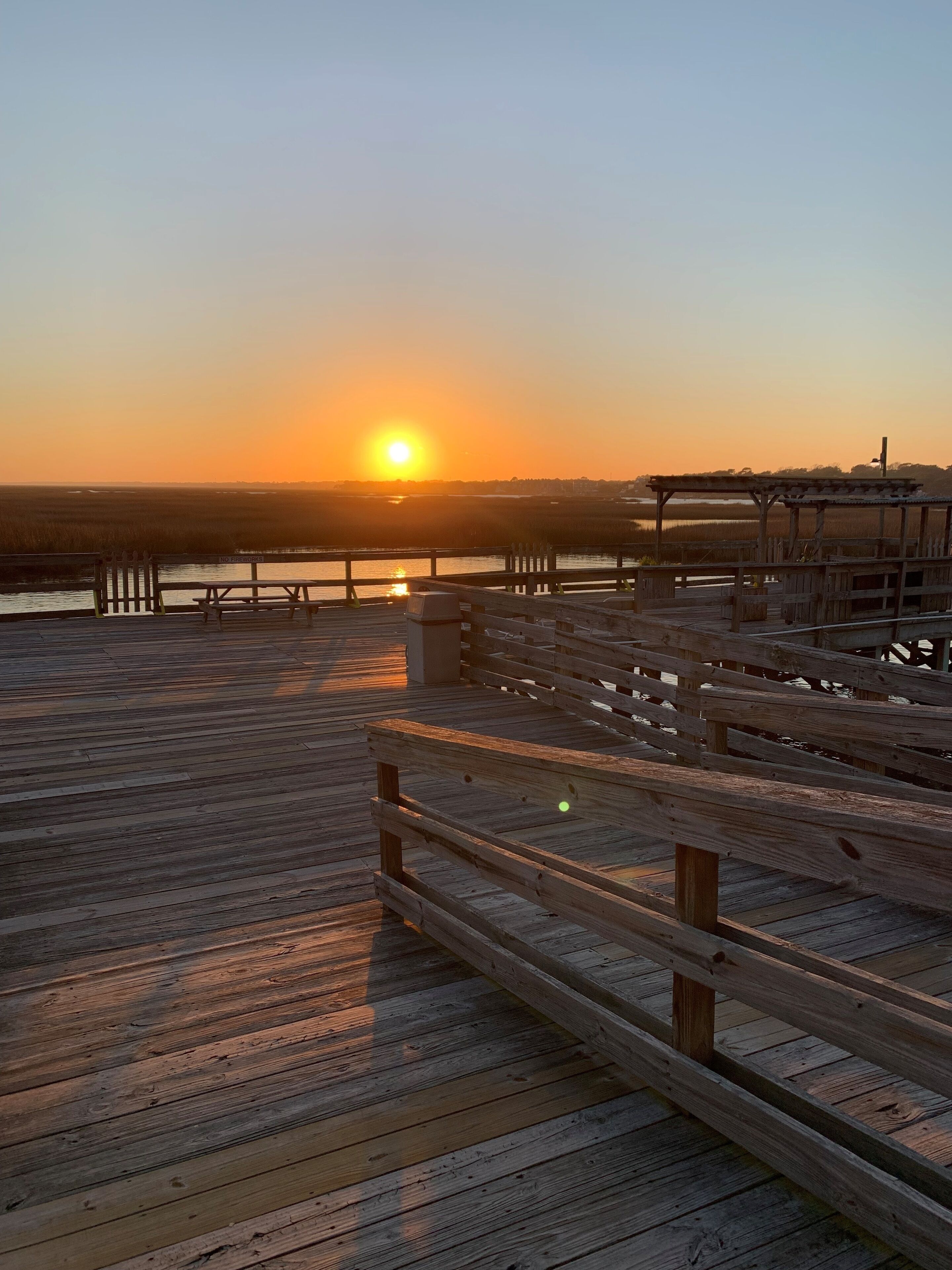 A wooden pier with benches and a gazebo, overlooking a body of water during sunset.