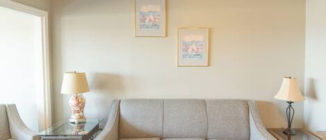 A living room with a grey sofa, two framed pictures on the wall, and two lamps on side tables.