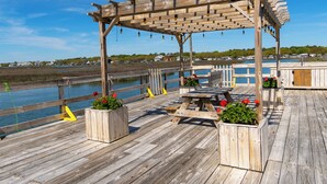 A wooden deck with a pergola, picnic tables, and planters with flowers. - Seawatch Inn at the Landing (Murrells Inlet)
