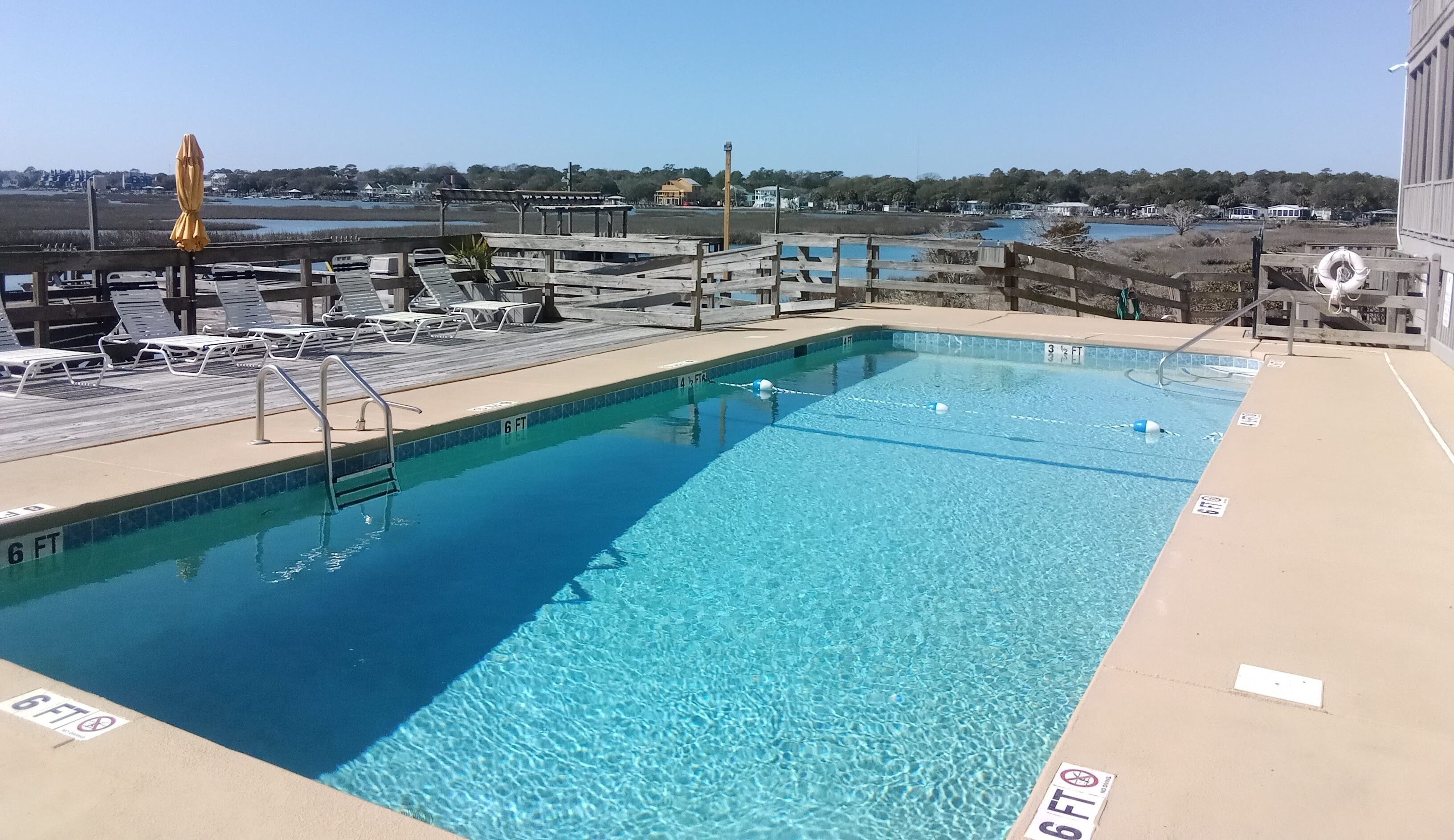 Une piscine aux eaux cristallines, dont la profondeur maximale est indiquée à 6 pieds, entourée de chaises longues et d’une terrasse en bois.