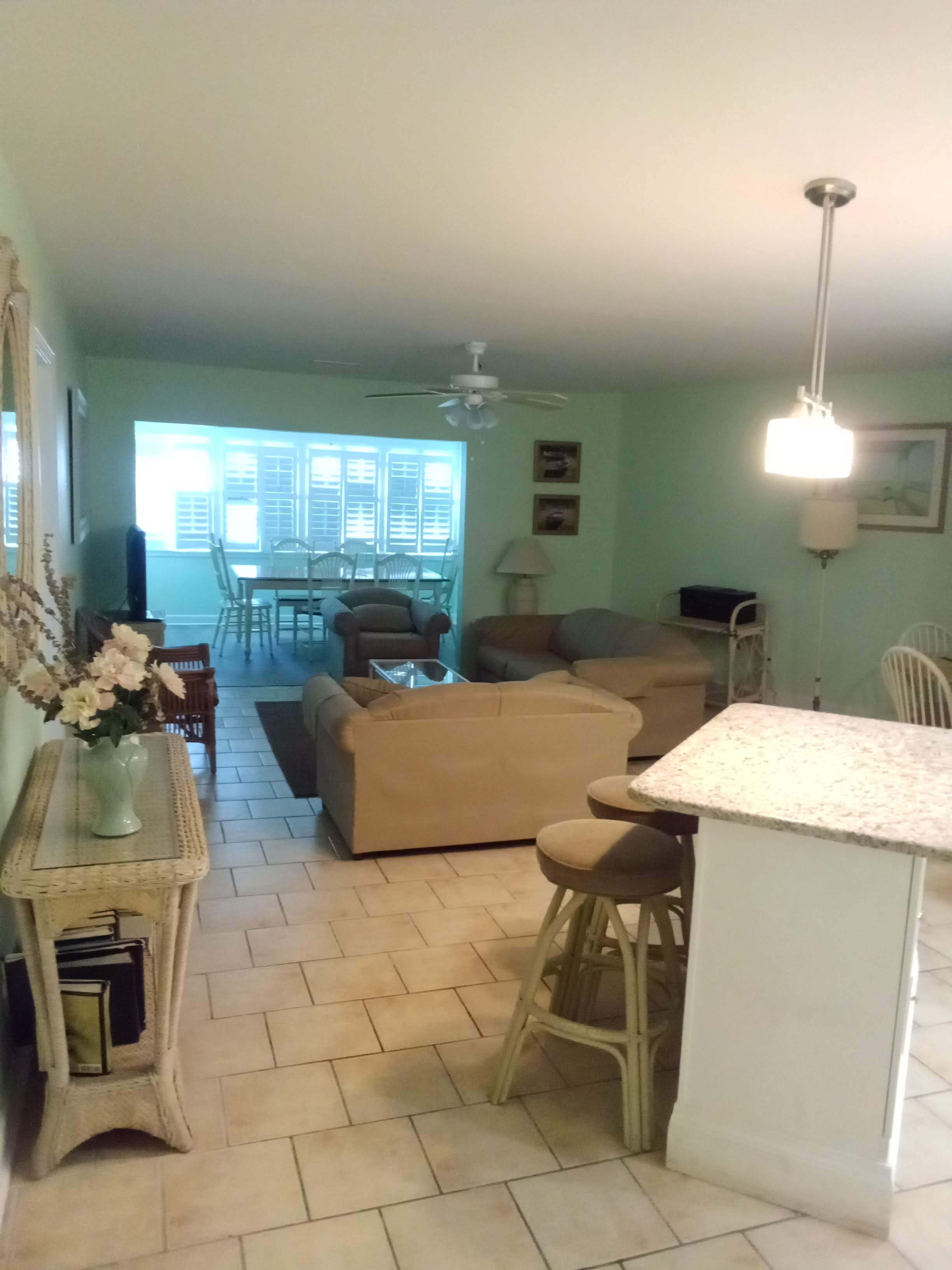 A living room with a sofa, a dining table, and chairs. There is a kitchen area with a counter and stools.