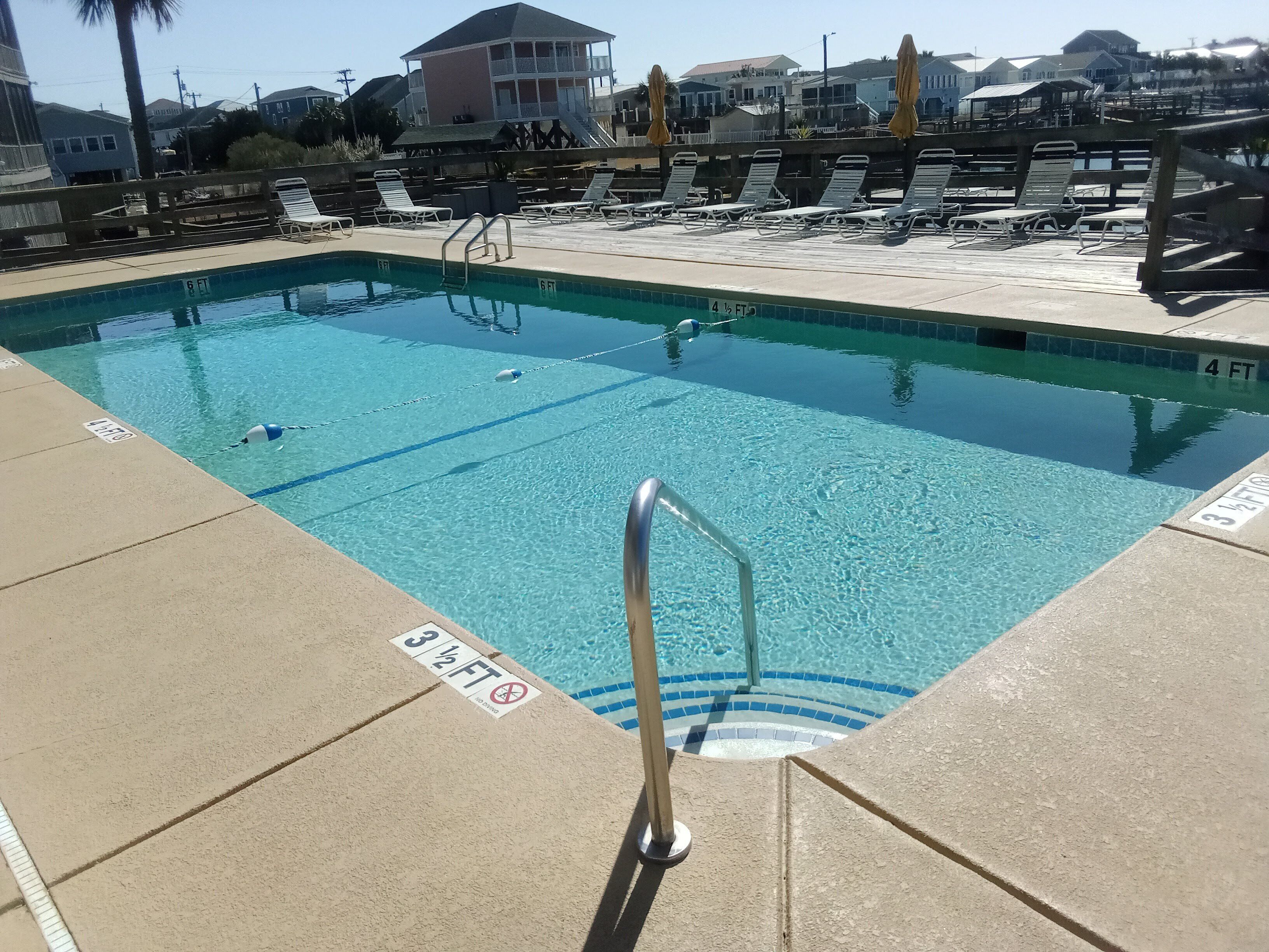 A swimming pool with clear water, marked depth lines, and a lifeguard stand.