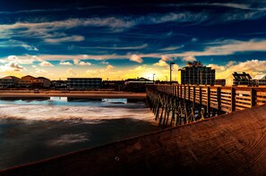 A wooden pier extending into calm waters with a sunset in the background and buildings on the shore. - Seawatch Inn at the Landing (Murrells Inlet)