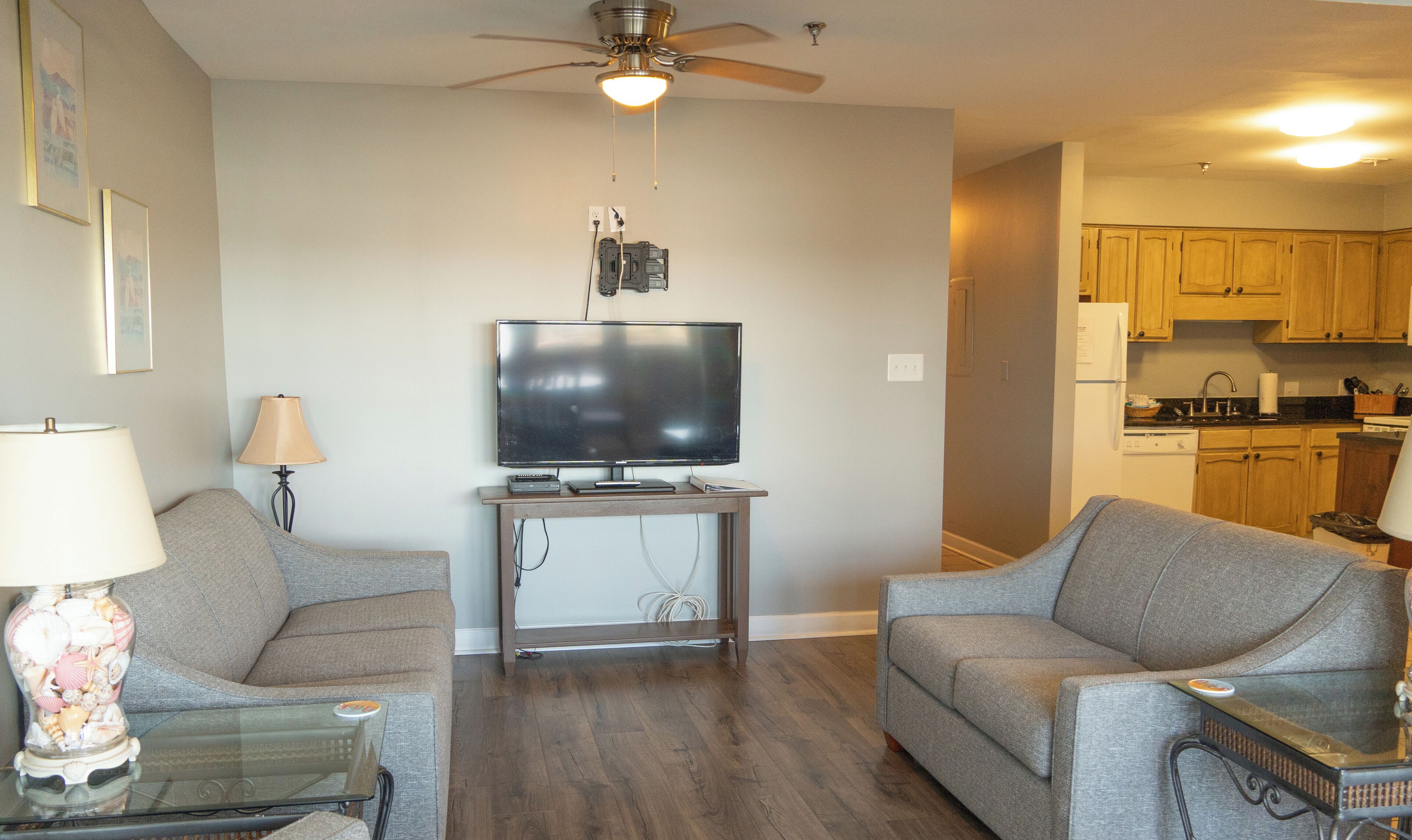 A living room with a flat-screen TV, two grey sofas, a coffee table, and a lamp.