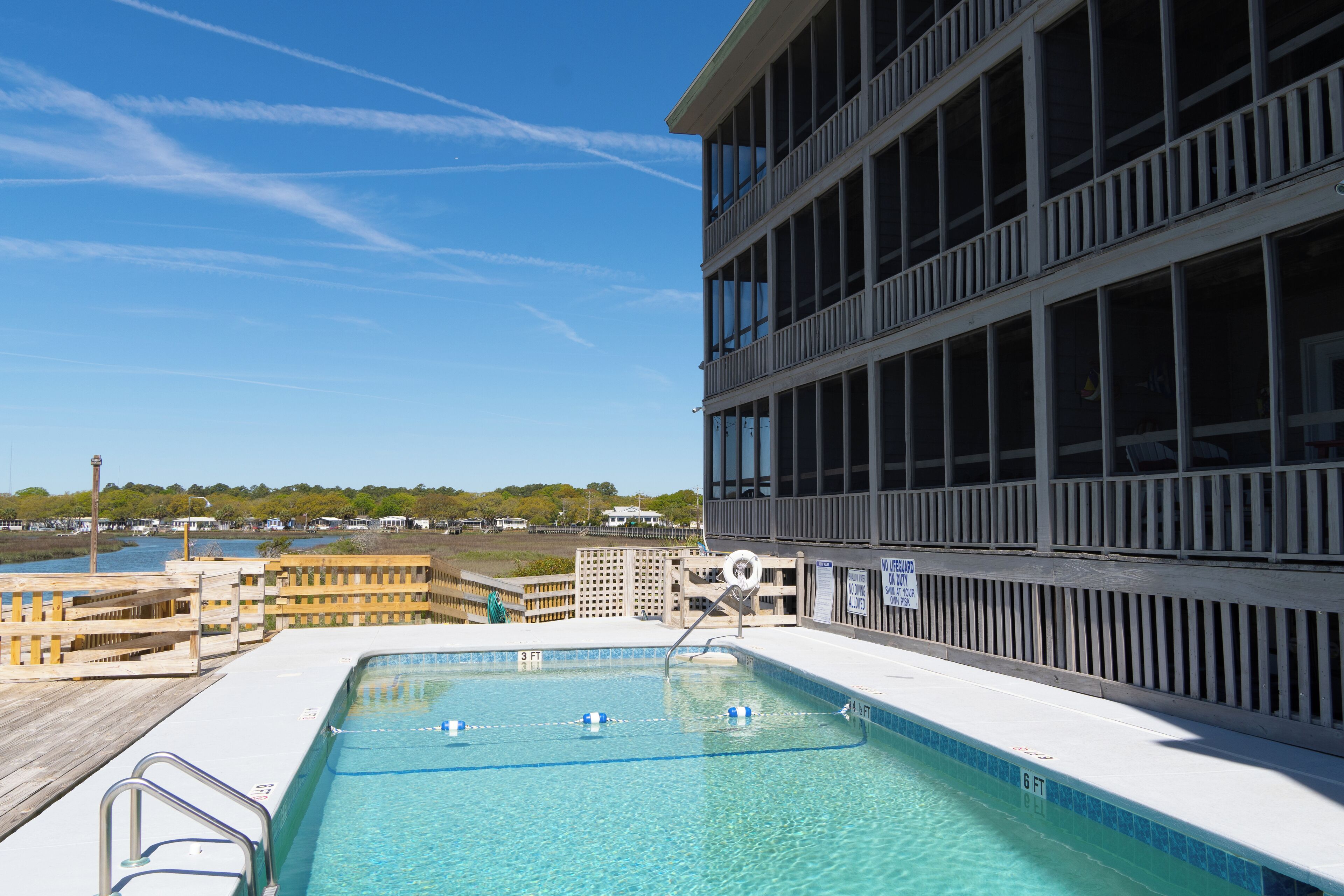 A swimming pool with a wooden deck, a lifeguard stand, and a view of a building with multiple windows.