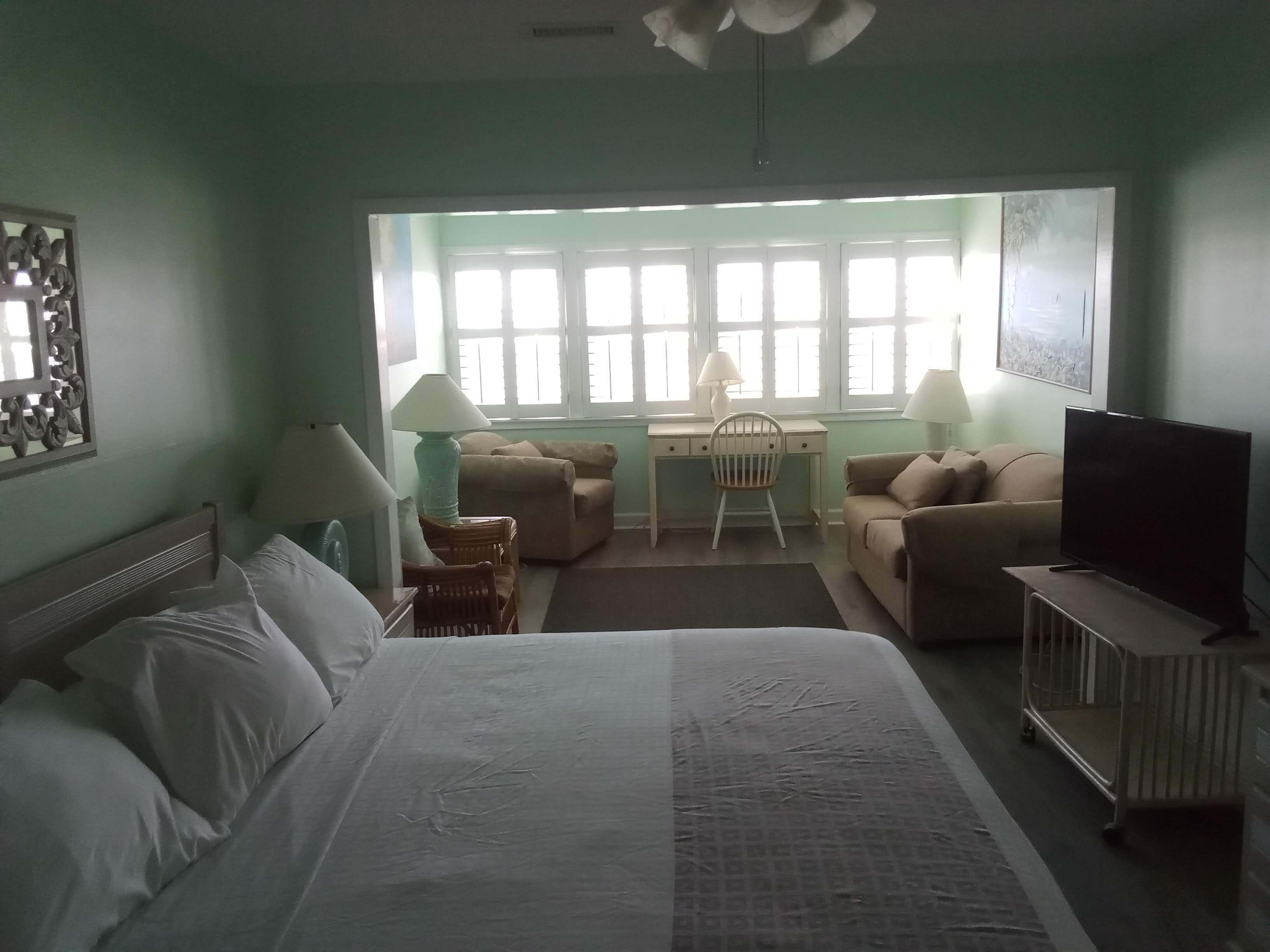 Une chambre d’hôtel équipée d’un lit, d’un bureau, de deux chaises, d’une télévision et d’une fenêtre avec des stores.