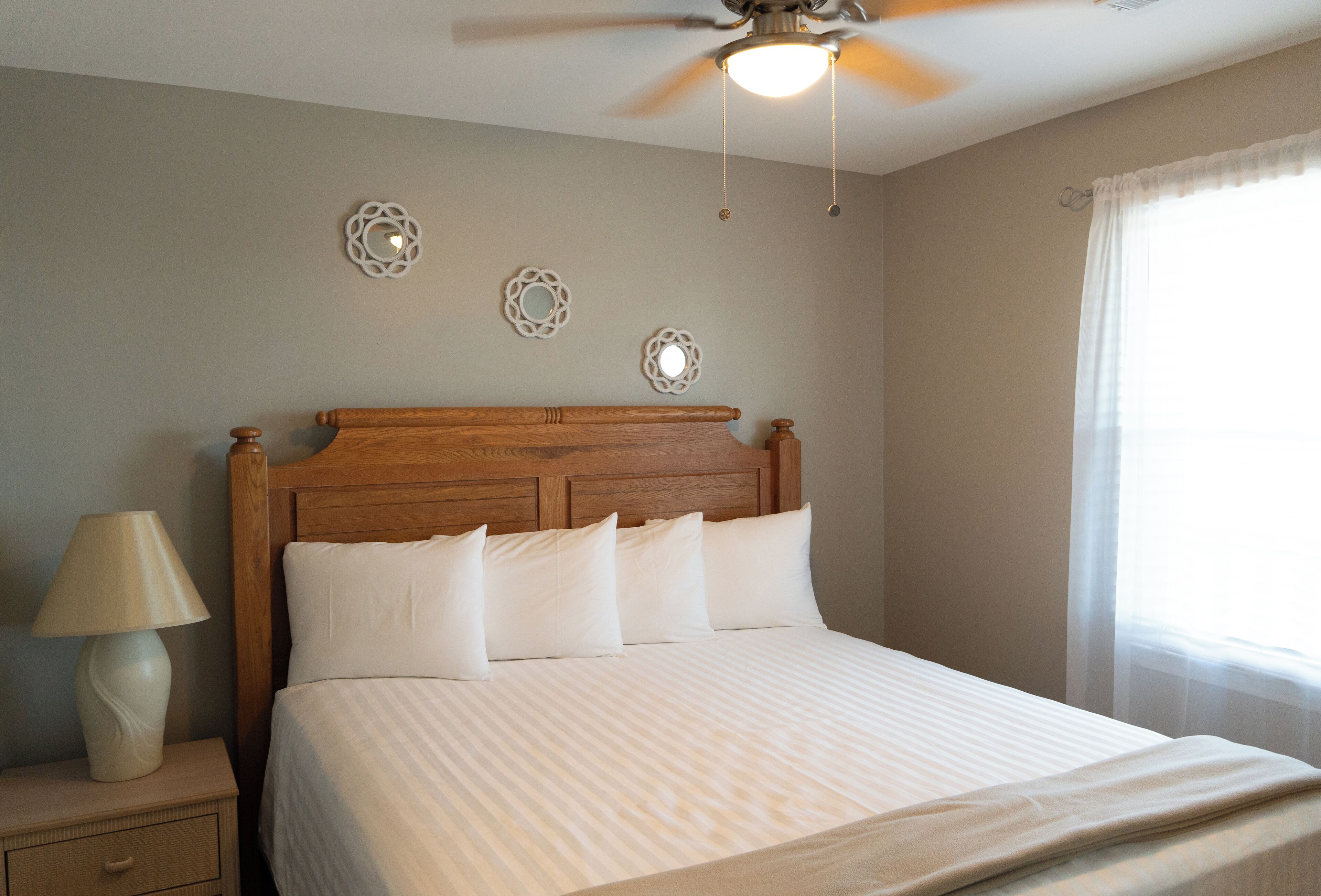 A neatly made bed with a wooden headboard, a bedside lamp, and decorative wall mirrors.