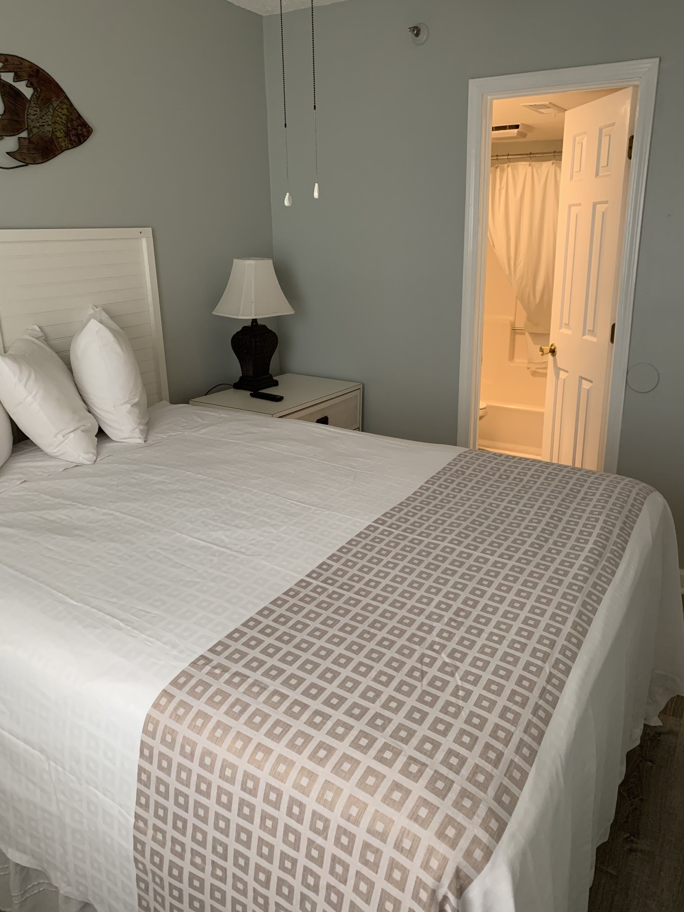 A bedroom with a bed, white headboard, bedside lamp, and a door leading to a bathroom.