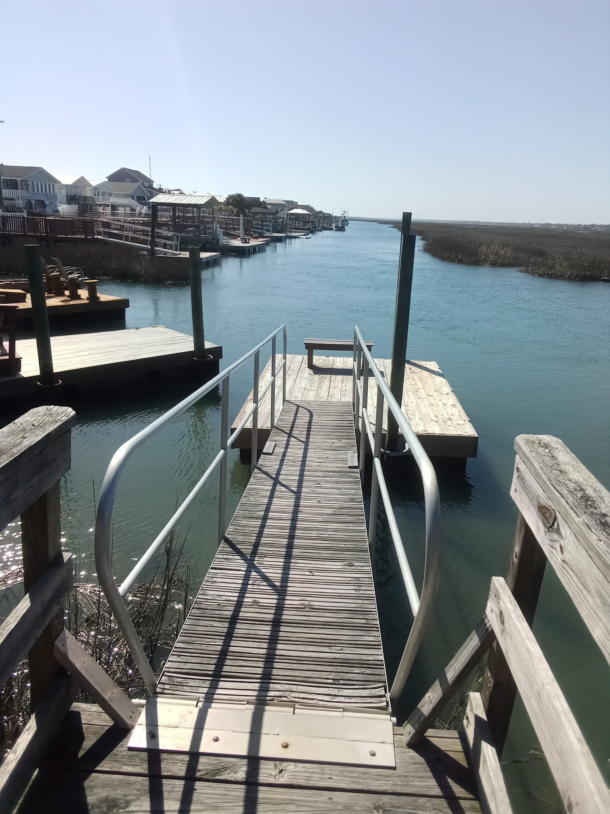 A wooden pier leading to a dock with a clear view of the water and distant buildings.