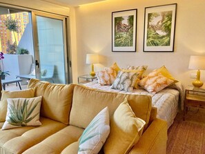 A hotel room with a sofa, a bed with patterned pillows, two bedside lamps, and two framed pictures on the wall.