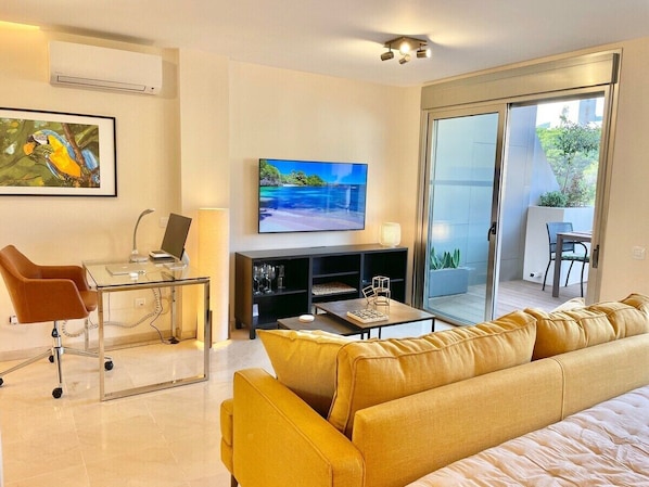 A modern living room with a sofa, a glass coffee table, a TV, and a laptop on a desk.