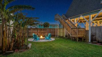 A backyard with a fire pit, two chairs, and a wooden deck.