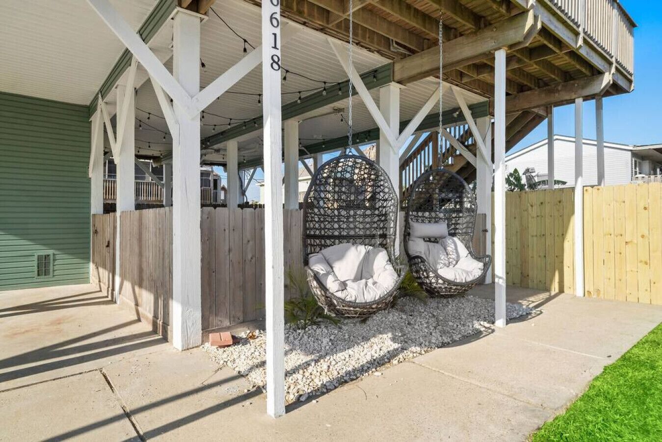 A covered porch with two wicker swing seats, a wooden fence, and a house number 0618.