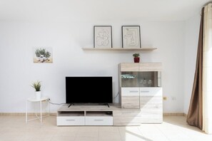 Ein modernes Wohnzimmer mit einem Flachbildfernseher, einem kleinen weißen Tisch mit einer Pflanze, einer Vitrine und zwei gerahmten Kunstwerken an der Wand.