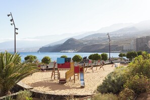 A beach with playground equipment, a clear view of the sea, and distant mountains.