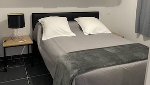 A bedroom with a bed, bedside table, lamp, air conditioning unit, and wooden cabinets. - Residence Pasturella, Large studio 30m2, swimming pool, countryside (BASTIA)