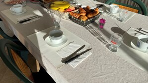 A breakfast table set with plates, cutlery, a basket of croissants, and a fruit bowl. - Residence Pasturella, Large studio 30m2, swimming pool, countryside (BASTIA)