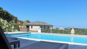 A poolside area with a lounge chair, a swimming pool, and a view of a building and trees. - Residence Pasturella, Large studio 30m2, swimming pool, countryside (BASTIA)