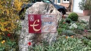 A garden with a large rock, various plants, and a sign with text. - Weingut & Gästehaus Andreas Erz (Brauneberg)