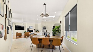 A modern kitchen with a central island, a dining area with chairs, a ceiling fan, and a large window with blinds. - Luxury Courtyard Home w/ Heated Pool/Spa & In-law Suite, 2 Min Walk to Beach! (New Smyrna Beach)