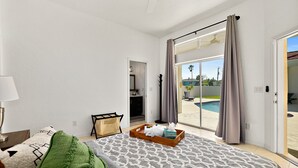 A bedroom with a bed, a bedside table, a lamp, a window with curtains, and a view of a swimming pool. - Luxury Courtyard Home w/ Heated Pool/Spa & In-law Suite, 2 Min Walk to Beach! (New Smyrna Beach)