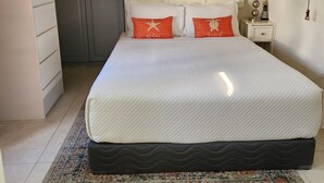 Un dormitorio ordenado con una cama, una mesita de noche, una lámpara y un cuadro en la pared.