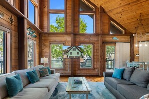 A spacious log cabin interior with large windows, a cozy seating area, and a view of a green house outside. - Weeki River Lodge Star5vacations (Spring Hill)