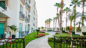 A pathway leading to a building with balconies, surrounded by palm trees and a pool. - BEAUTIFUL CONDO 2BD 3 MIN FROM BEACH AND DOWNTOWN (Cabo San Lucas)