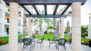 An outdoor patio with stone columns, metal chairs, and tables. - BEAUTIFUL CONDO 2BD 3 MIN FROM BEACH AND DOWNTOWN (Cabo San Lucas)