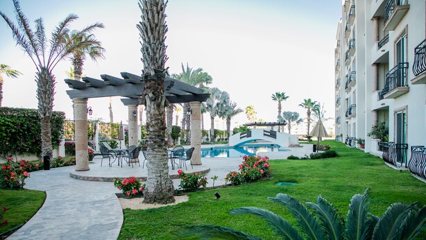 A resort with a swimming pool, palm trees, and outdoor seating areas. - BEAUTIFUL CONDO 2BD 3 MIN FROM BEACH AND DOWNTOWN (Cabo San Lucas)
