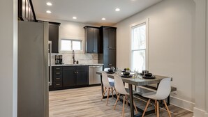 Una cocina moderna con armarios oscuros, encimera de mármol y comedor con mesa y sillas.