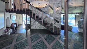 Ein großzügiger Innenraum mit einer Steinwand, einer Holztreppe und einem großen Kronleuchter.