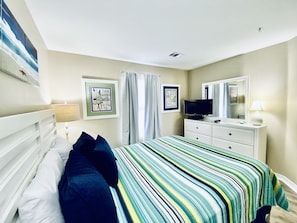 Un dormitorio con una cama, un aparador, un televisor y dos cuadros en la pared.