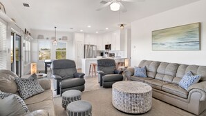 Un salon moderne avec un canapé, des fauteuils, un pouf et un ventilateur de plafond.
