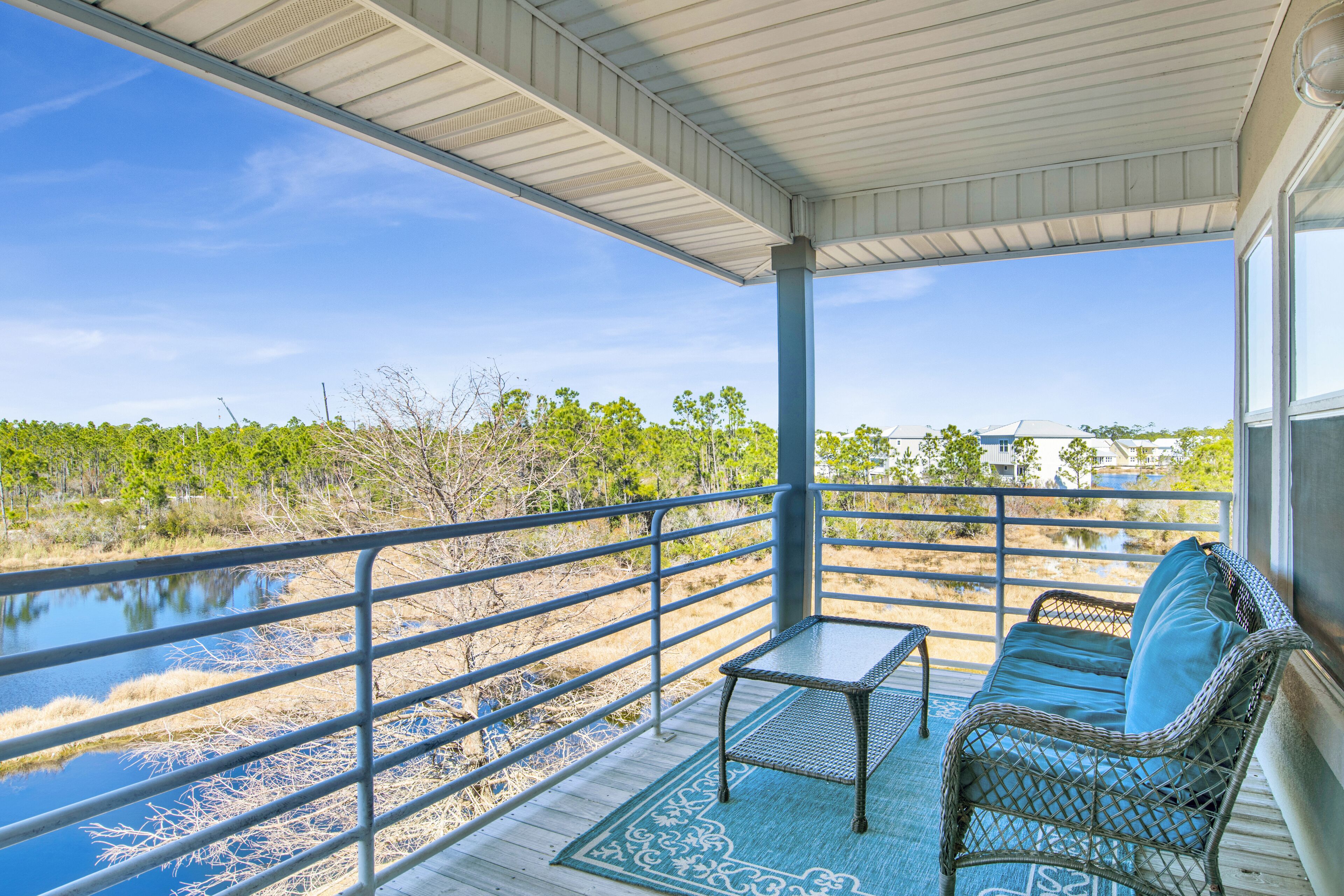 A covered balcony with a view of a water body and vegetation, a wicker sofa, and a small table.