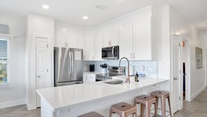 Une cuisine moderne avec des meubles blancs, des appareils en acier inoxydable et un îlot central doté de tabourets.