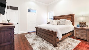 A bedroom with a large bed, wooden headboard, white walls, and a wooden dresser. - Lux Brand New! Beautiful House w/ Pool & Hot Tub (New Orleans)