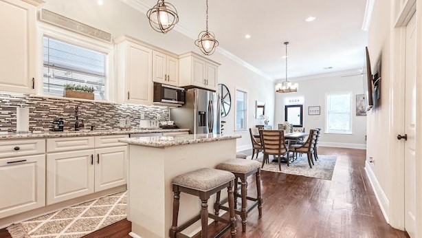 A spacious kitchen with a large island, wooden bar stools, and a dining area with a table and chairs. - Lux Brand New! Beautiful House w/ Pool & Hot Tub (New Orleans)