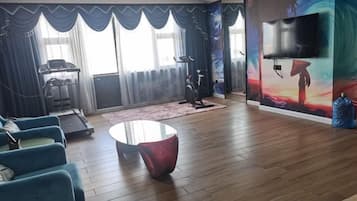 Una habitación con una cinta de correr, una bicicleta estática y una televisión grande en la pared.