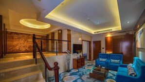 A modern living room with a staircase, blue sofas, and a patterned carpet. - Rodin Oswey Hotel (Luoding)