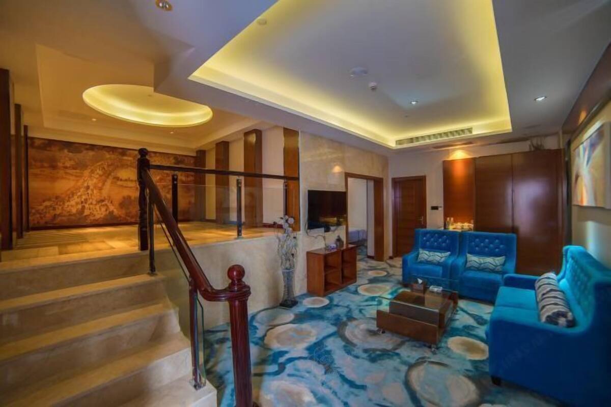 A modern living room with a staircase, blue sofas, and a patterned carpet.