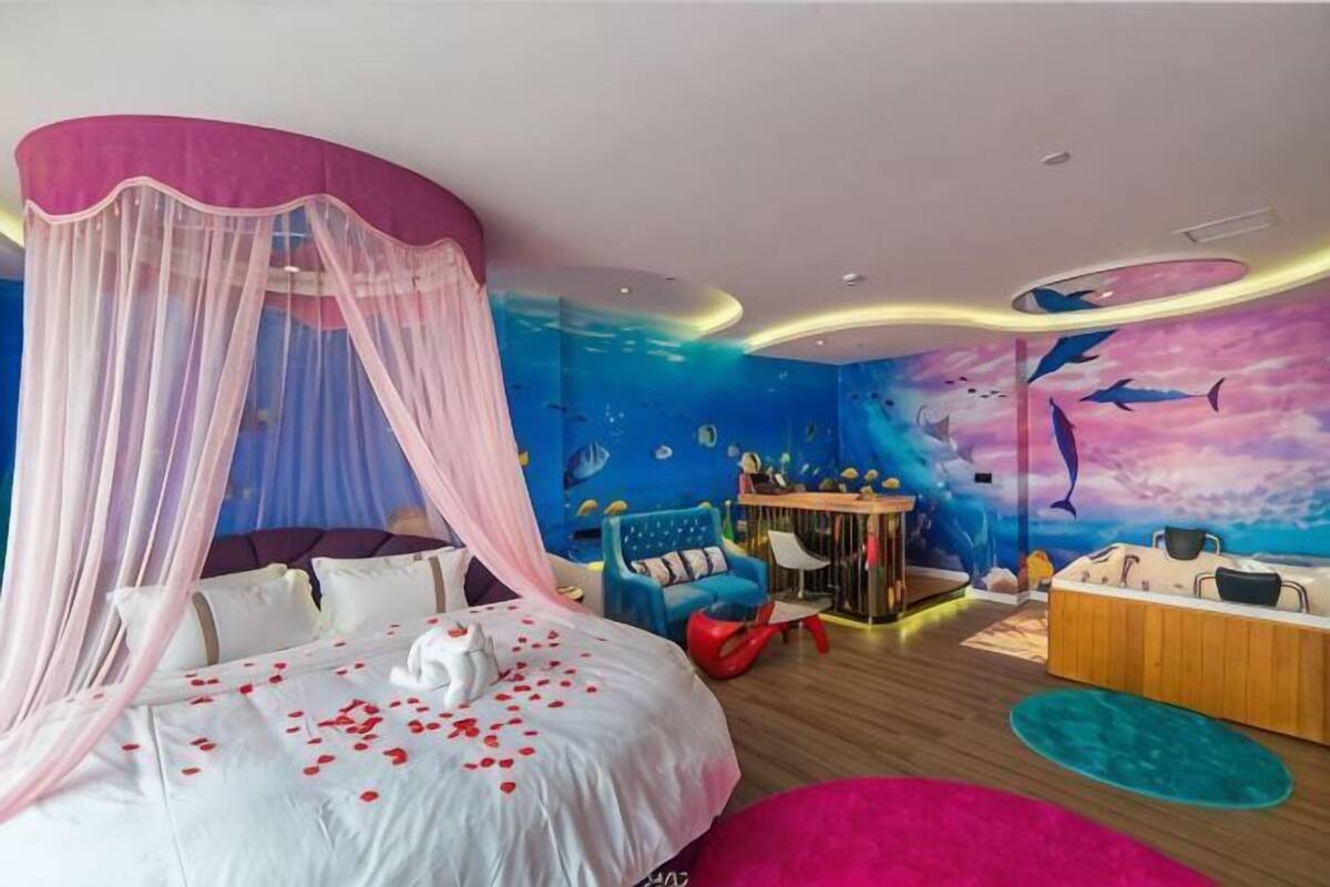 A bedroom with a bed, a vanity, a desk, and a wall mural.