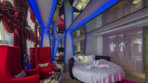 A modern hotel room with a large bed, a red armchair, a glass coffee table, and a view of the city through large windows. - Rodin Oswey Hotel (Luoding)